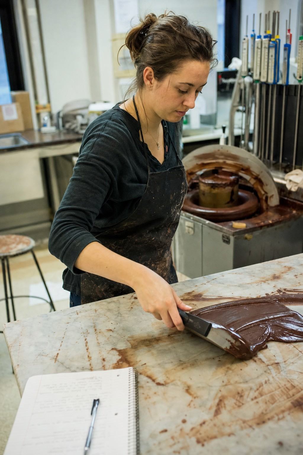 UT graduate student Renee Whitlow tempers chocolate on a marble slab in a small campus lab, with a melanger and analog thermometers behind her.