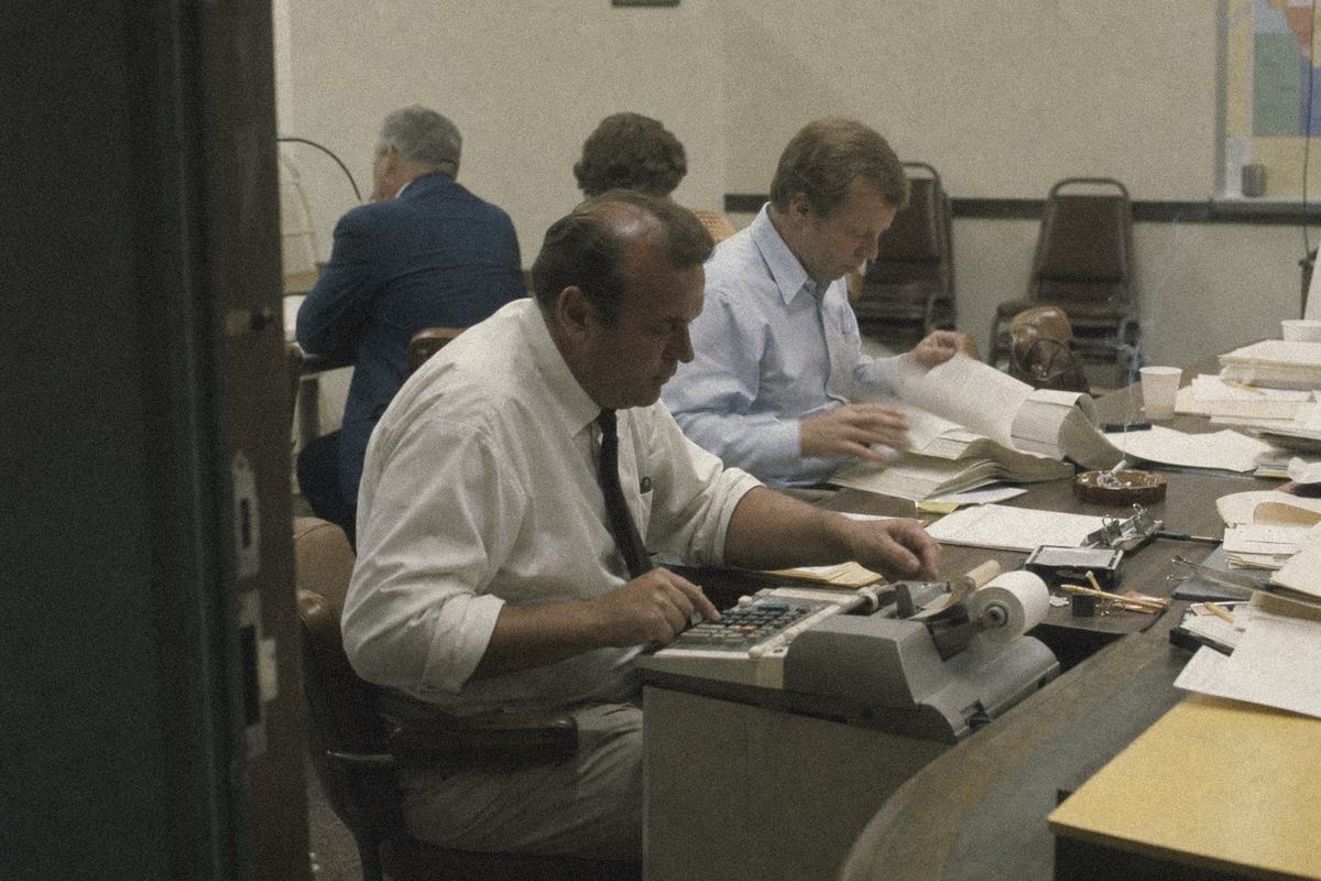 County supervisors lean over ledgers and an adding machine during a budget session in Peoria.