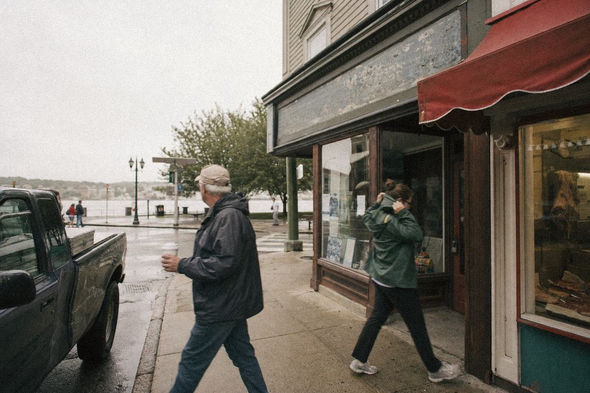 Street view of Bank Street on a gray morning, the Regatta Office storefront and the butcher’s awning with the river glimpsed down the cross street.