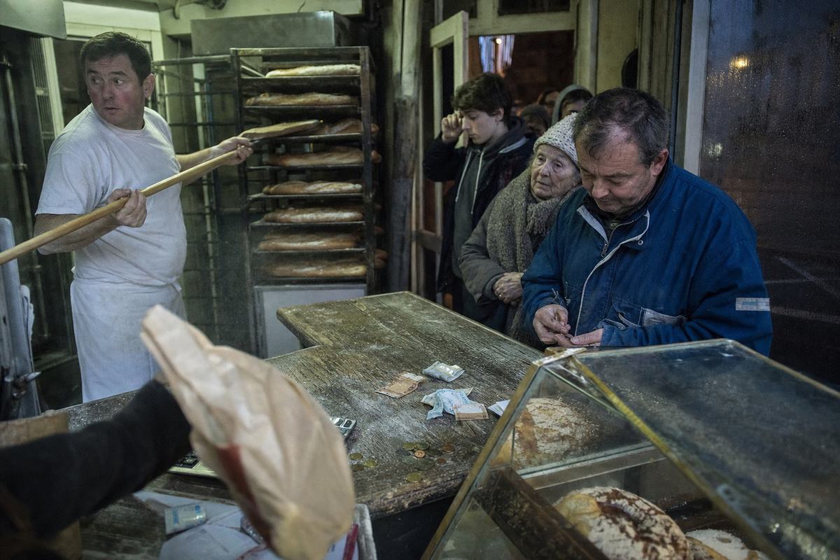 À la Boulangerie du Velay, avant l’aube: file serrée devant le comptoir, le boulanger en pleine fournée, billets froissés sur le bois.