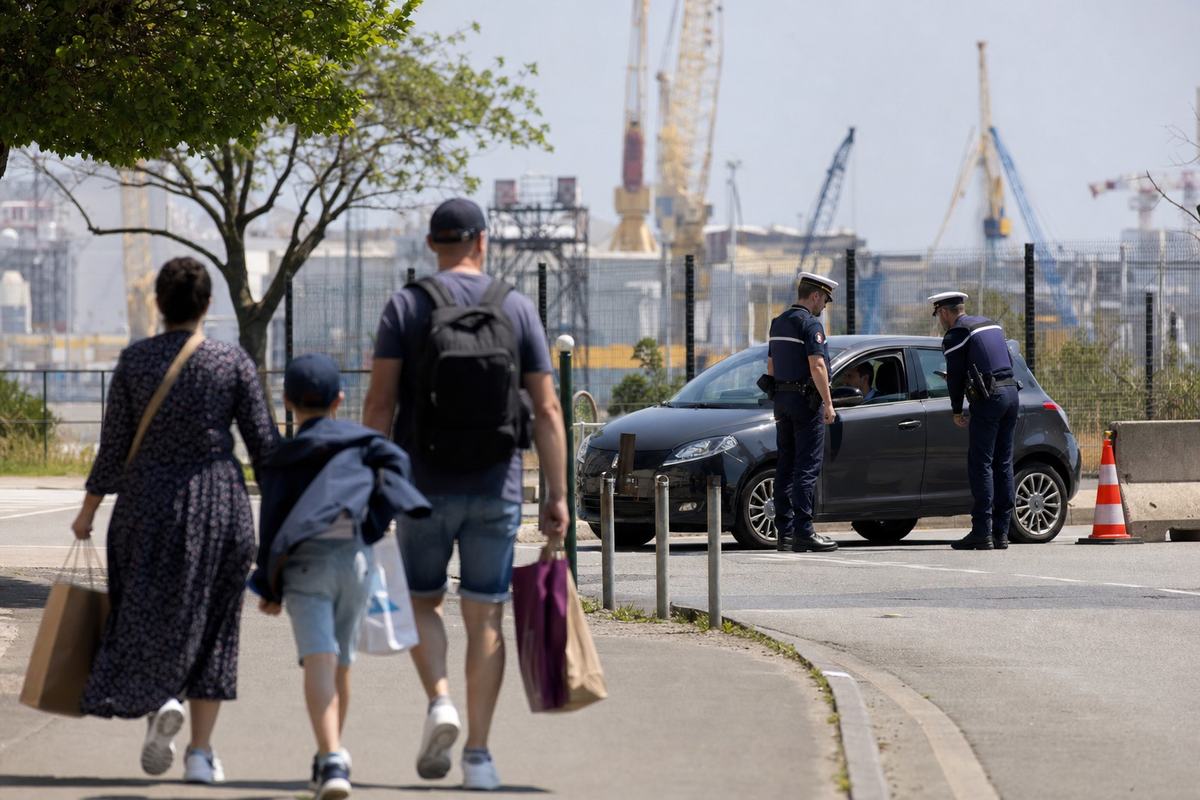 À l’entrée de la base navale de Brest, vue depuis la voie publique: gendarmes maritimes au point de contrôle, passants avec des sacs de courses.
