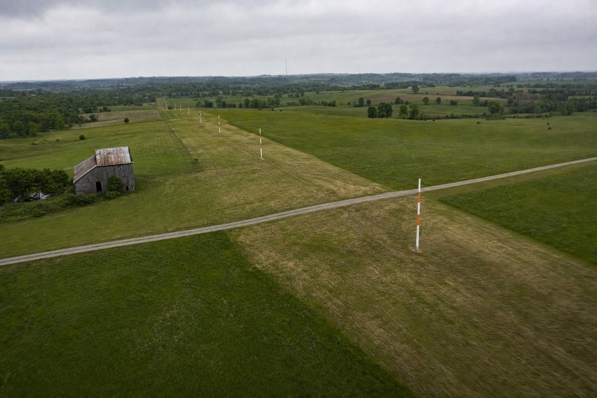 Oblique aerial of the easement stripe across hayfields east of Caldwell, with height-limit markers and the mast on the horizon.