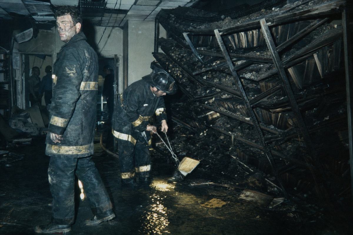 Interior view of the NPRC in 1973 with charred shelves, smoke damage, and firefighters moving through wet debris.