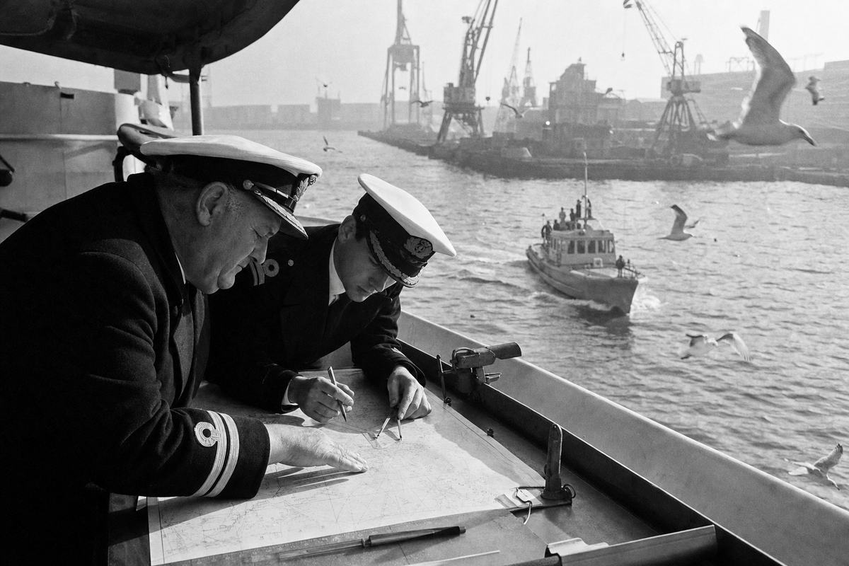 Black-and-white press photo of two naval officers leaning over a chart table aboard a patrol craft in Montevideo harbor during a joint drill, with labels not visible.