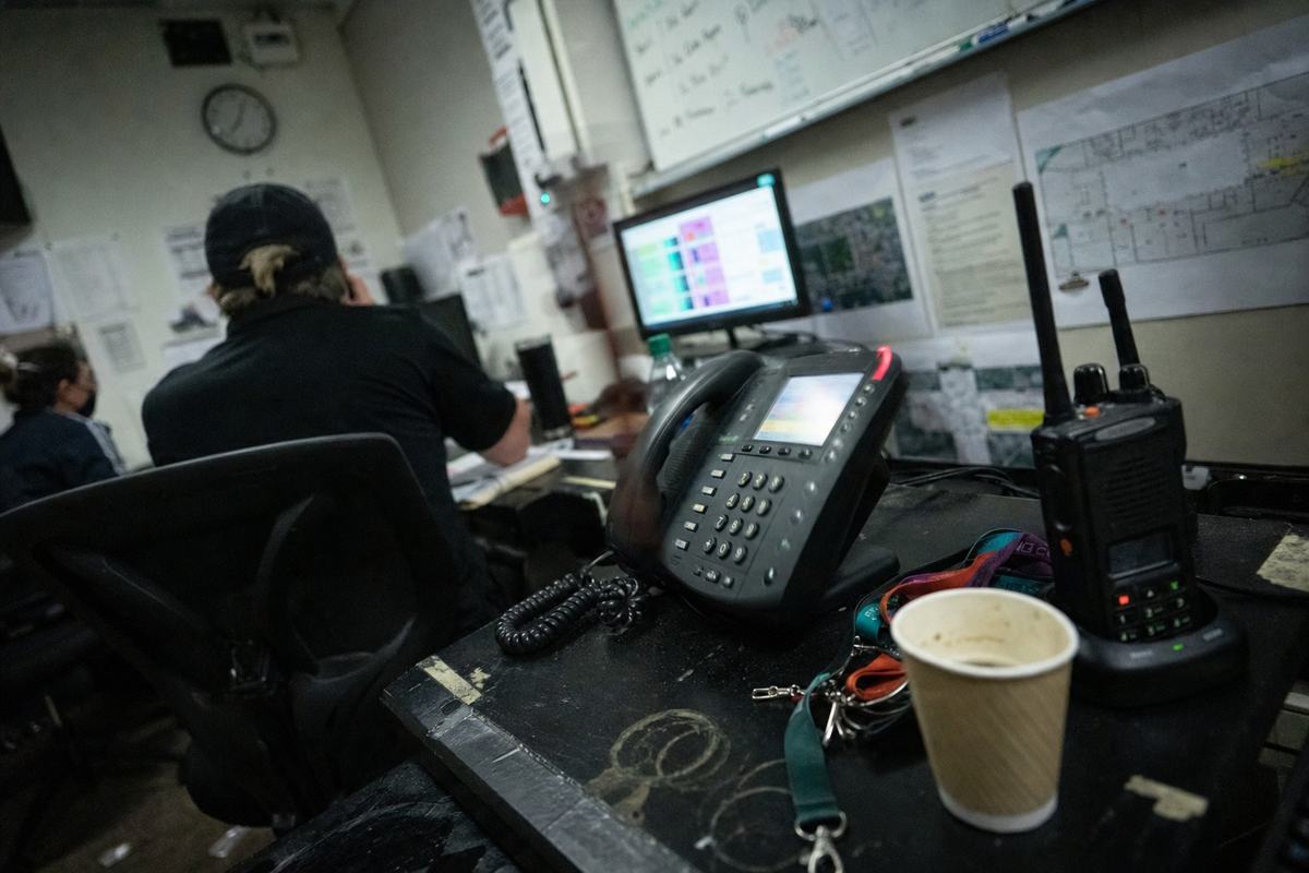 Venue operations desk with a ringing phone, radios, coffee cup rings, and out-of-focus floor plans pinned on the wall.