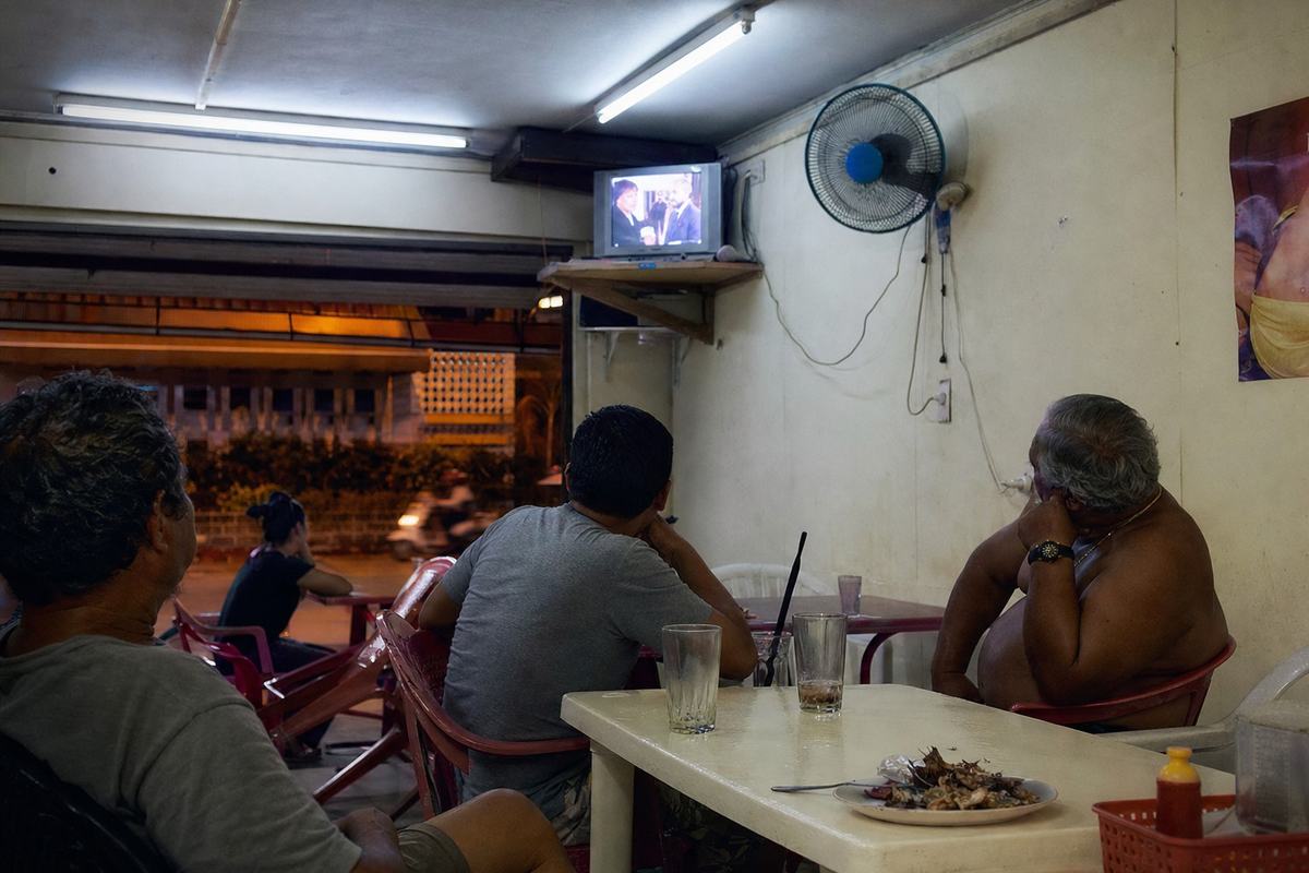 Téléviseur dans un snack de Papeete diffusant la minisérie; clients regardant, verres embués.