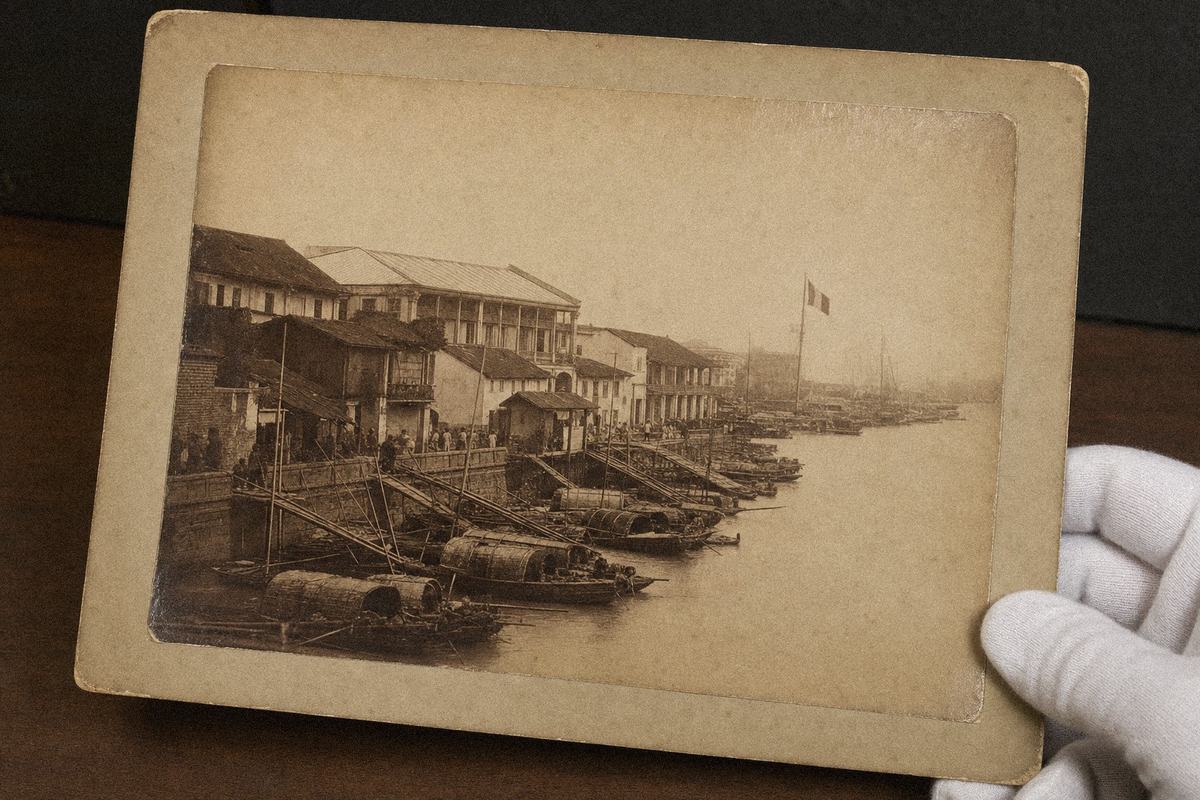 Reproduction d’un tirage albuminé des quais de Shamian, entrepôts, passerelles vers les sampans et pavillon français en tête de mât.
