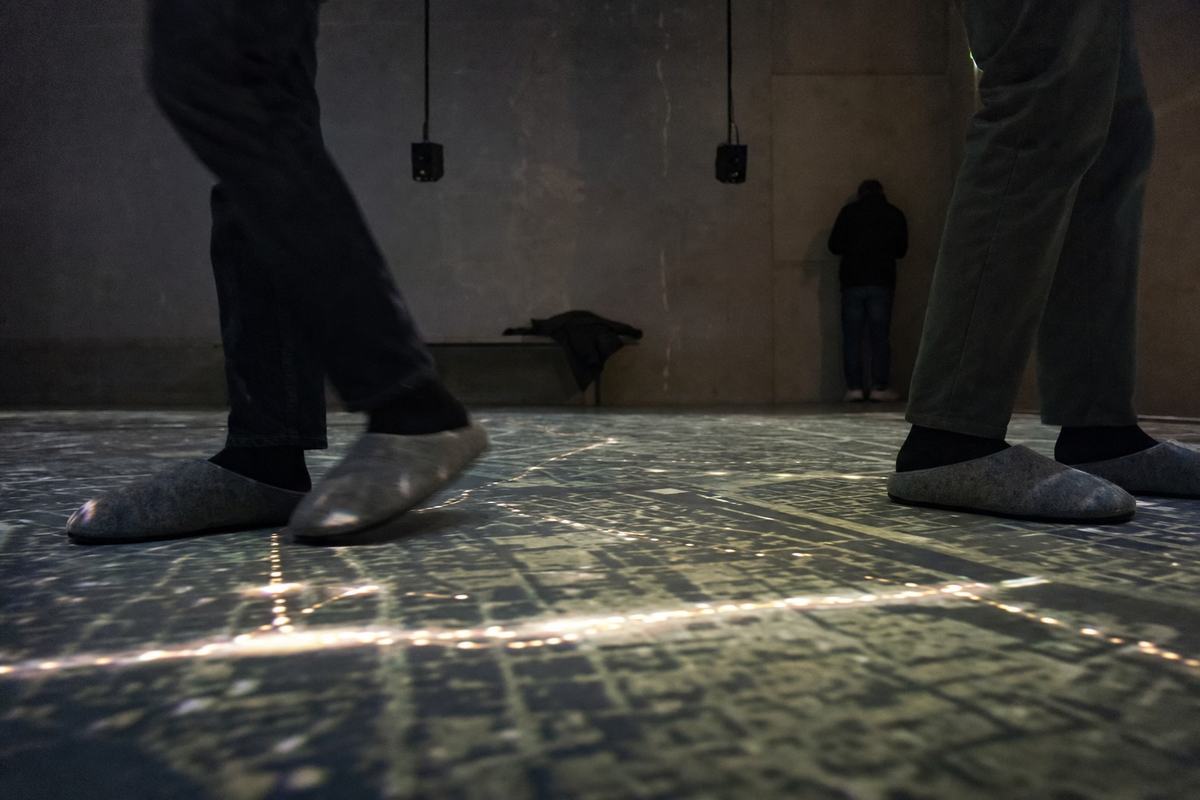 Salle d’écoute immersive, chaussons feutrés sur une carte projetée du Paris occupé, haut-parleurs suspendus.