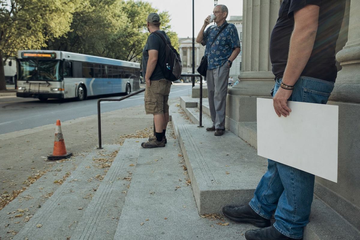 Outside the A.A. Birch courthouse, an idling bus and a few bystanders with lowered placards linger in the late-summer heat.