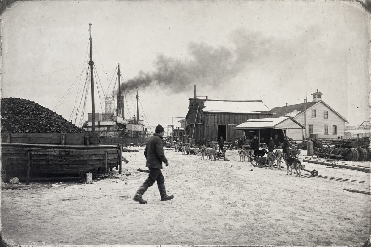 c. 1890s silver gelatin print made from an 8×10 dry plate negative at King William Settlement harbour; fine grain with rich midtones and crisp highlights on snow; camera at chest height with a ~150mm lens; asymmetric composition with coal stacks and a timber lighter at left, depot sheds and a small hospital building to the right, sled teams waiting in foreground; a single worker in a wool cap crosses the frame mid‑stride, slight motion blur at his boots; rigging from a moored steamer rises behind the depot; smoke drifts across the sky; scattered barrels and timber (turned so no labels or lettering are visible); wind‑scoured snow with boot tracks; edges show light silvering from age.