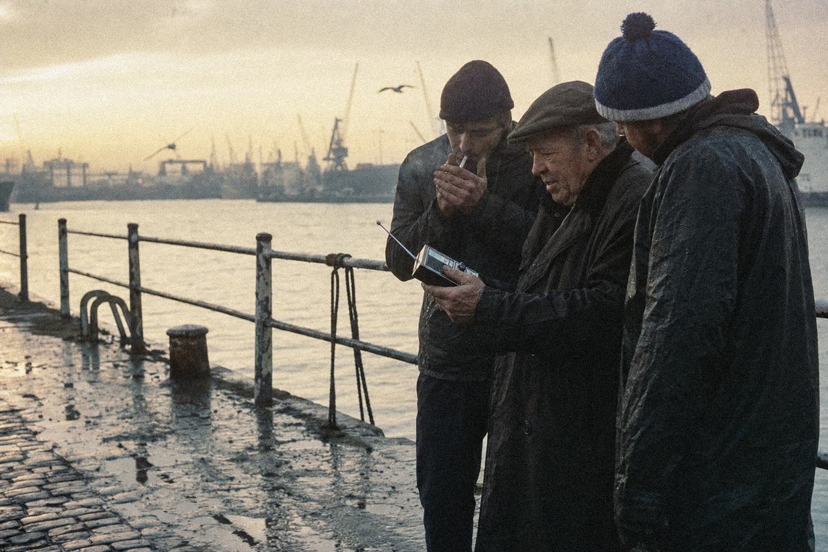 Fishermen at St Andrew’s Dock at dawn, listening to a small radio by the railings.