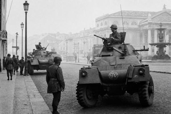 Black-and-white archival-style photograph of an early-morning GNR patrol with 1970s Portuguese armored cars near Lisbon's Rossio square in April 1974. Cobblestone streets under light fog, tense faces of uniformed troopers, period-accurate vehicles during the 'nuit interrompue.' Soft silver-gelatin film grain, documentary photojournalism aesthetic, background includes faint outlines of historical Lisbon architecture.