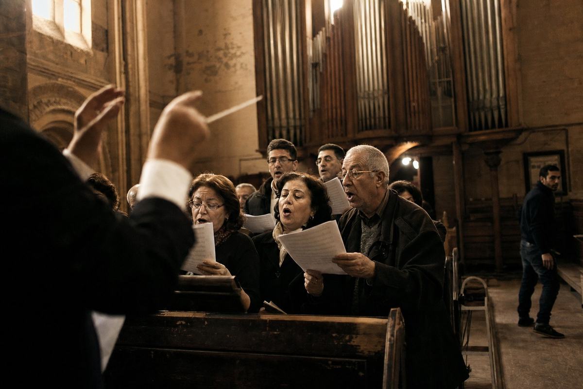 Répétition chorale au Sacré‑Cœur: mains du chef levées, tuyaux d’orgue au fond, chanteurs à demi flous.