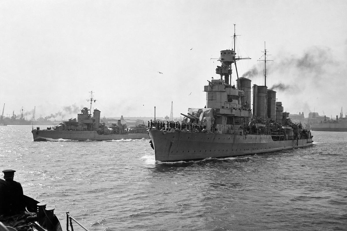 French cruisers under escort approach Alexandria harbor, smoke trailing as small waves break against their bows.