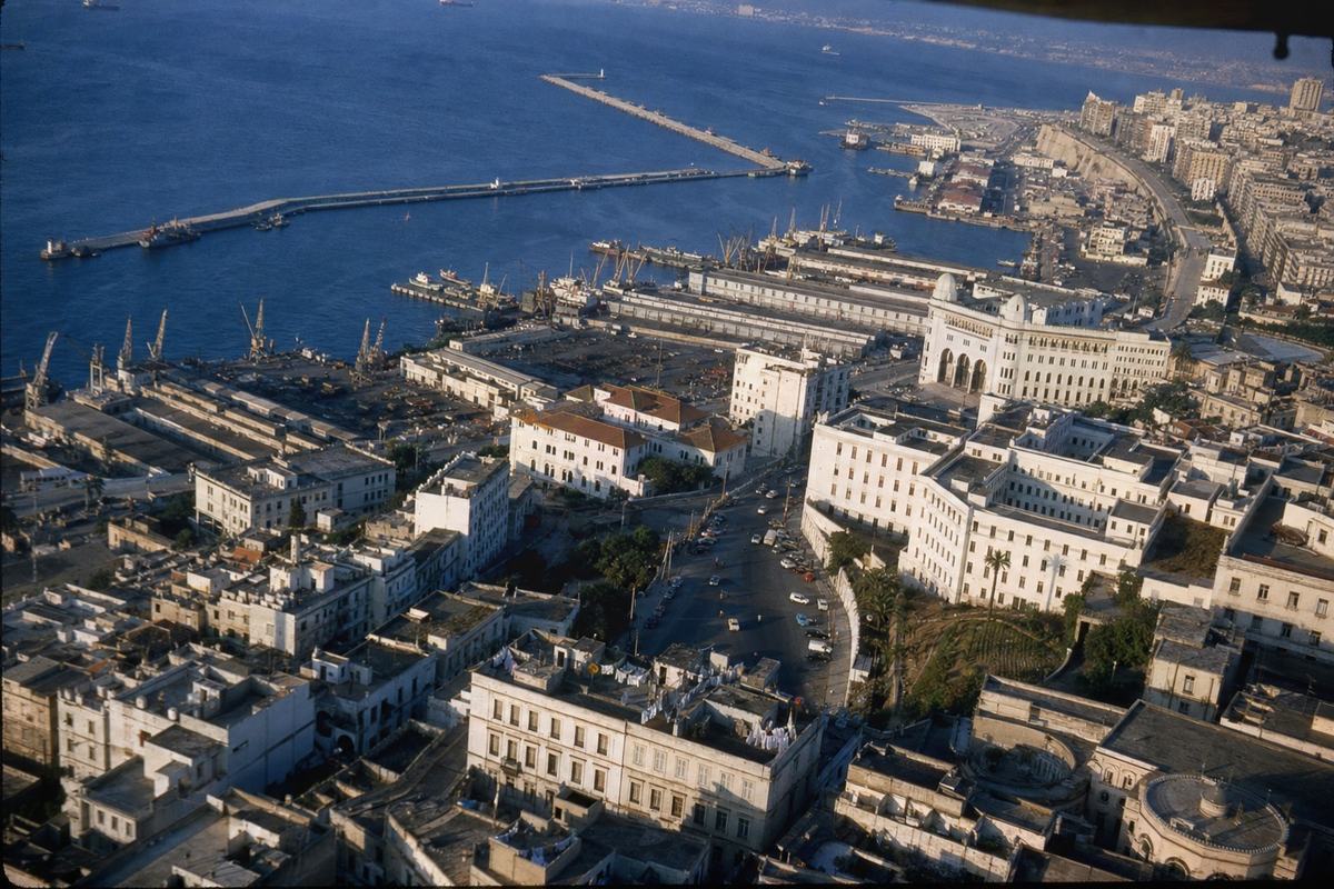 Oblique aerial view of Algiers’ ministries and harbor in the mid-1950s, with sunlit terraces and blue water.