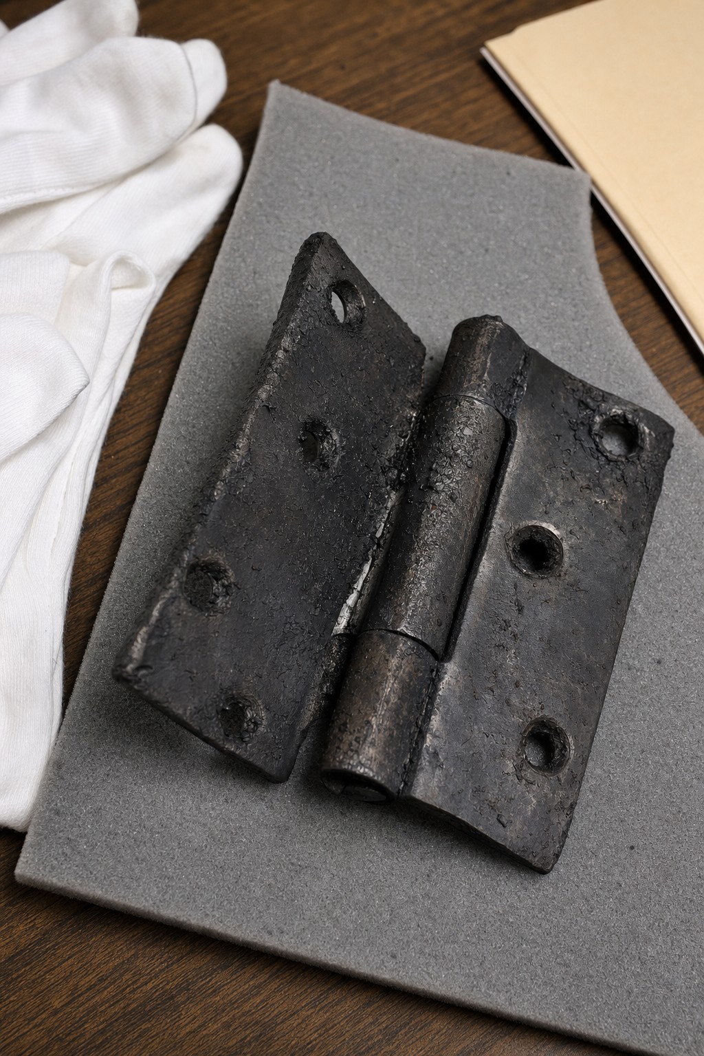 Charred iron door hinge from the R Street bombing, photographed on archival foam with cotton gloves nearby.