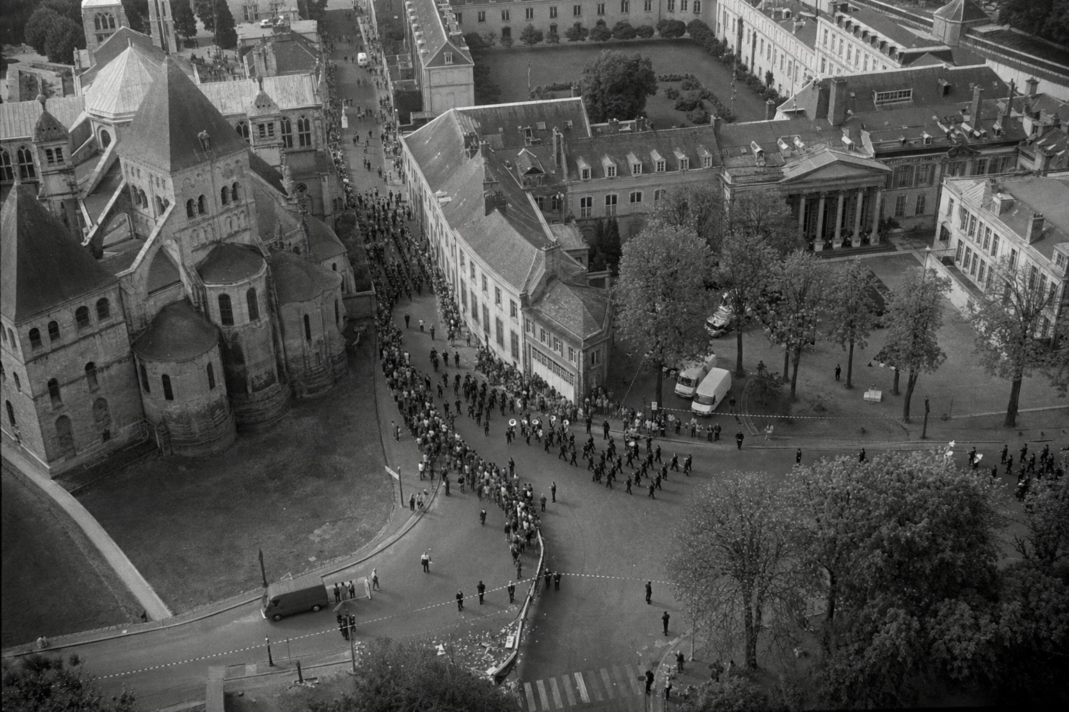 Vue aérienne en noir et blanc du quartier palatin de Compiègne, avec Saint‑Corneille, le palais, les Chambres et la Place des Plaids animée par les cortèges du millénaire.