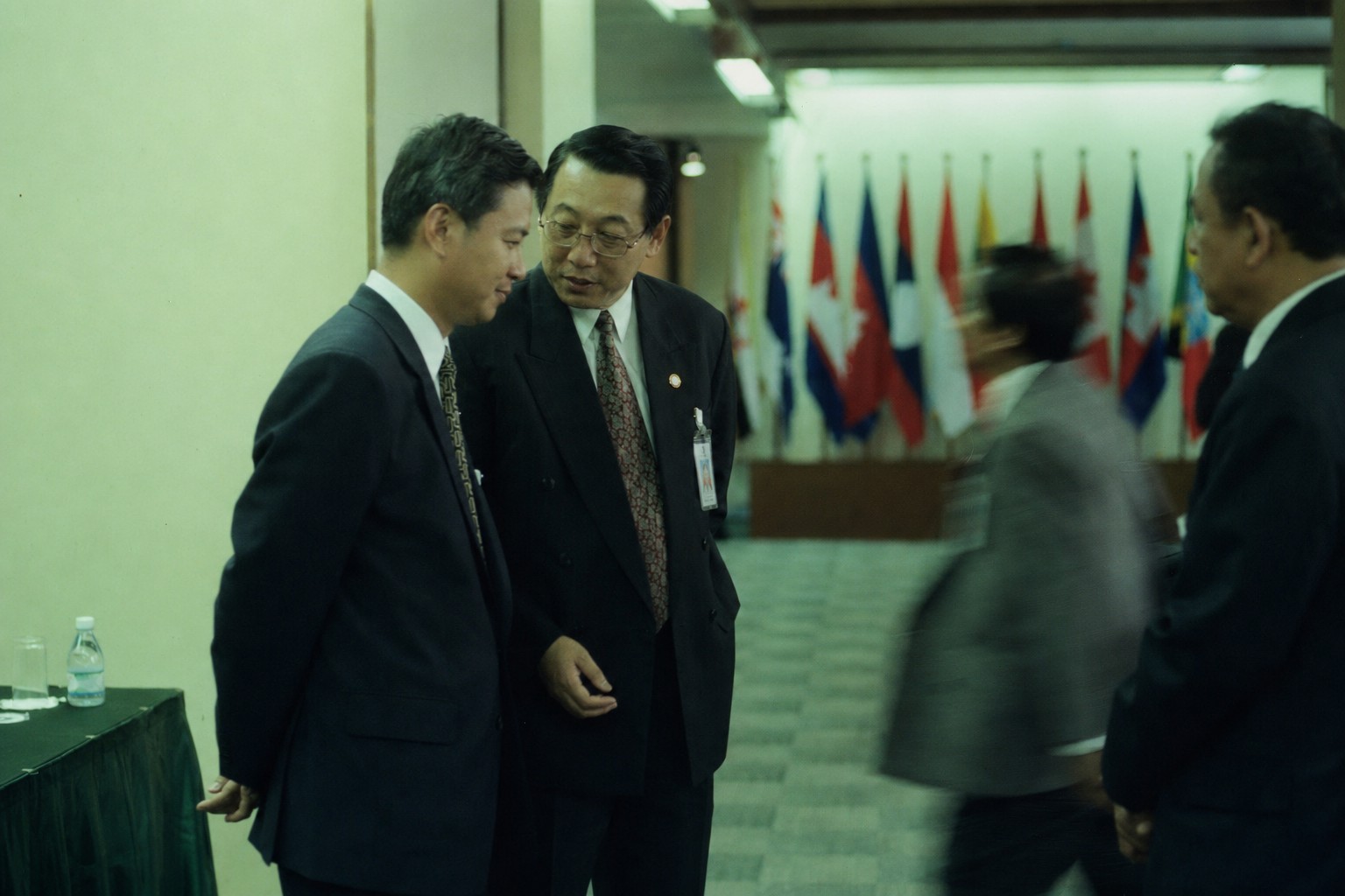 Delegates confer in a hallway at a Saigon-hosted ASEAN ministerial, flags blurred behind them, 1998.