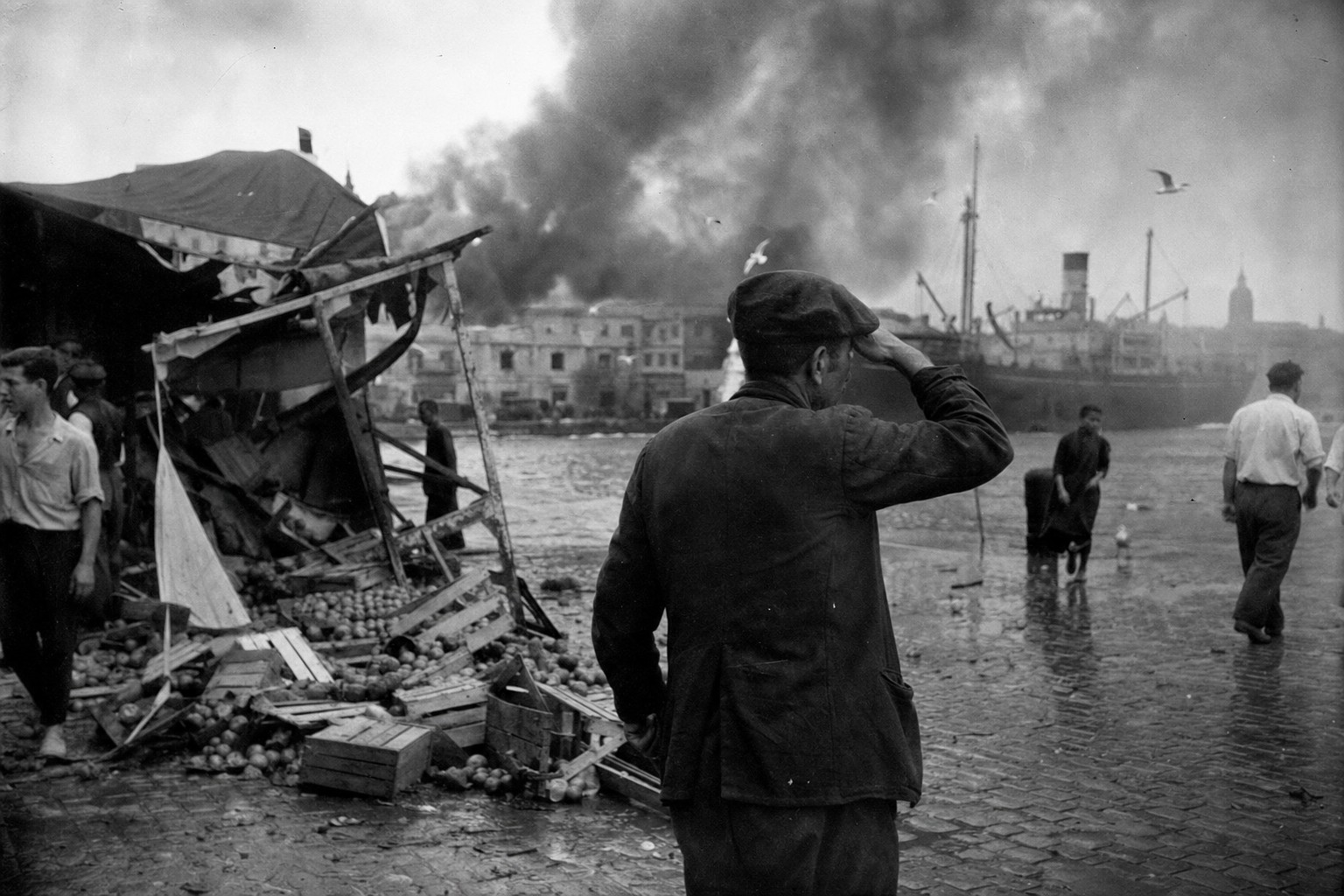 Smoke over Alicante’s market and harbor with a dockworker shielding his eyes, 25 May 1938